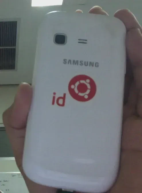 Seorang penerima stiker #SebarUbuntu tersenyum lebar menunjukkan stiker baru di dekat laptopnya